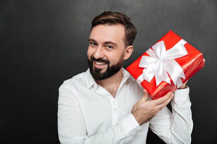 Portrait of Curious Man Shaking Wrapped Red Box and Trying to Recognize What's Inside Over Dark Gray Wall 171337 603